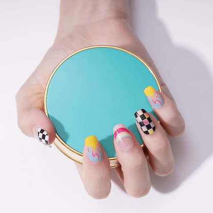 Hand holding turquoise compact mirror showcasing nail art wraps with black checkered and rainbow flame patterns