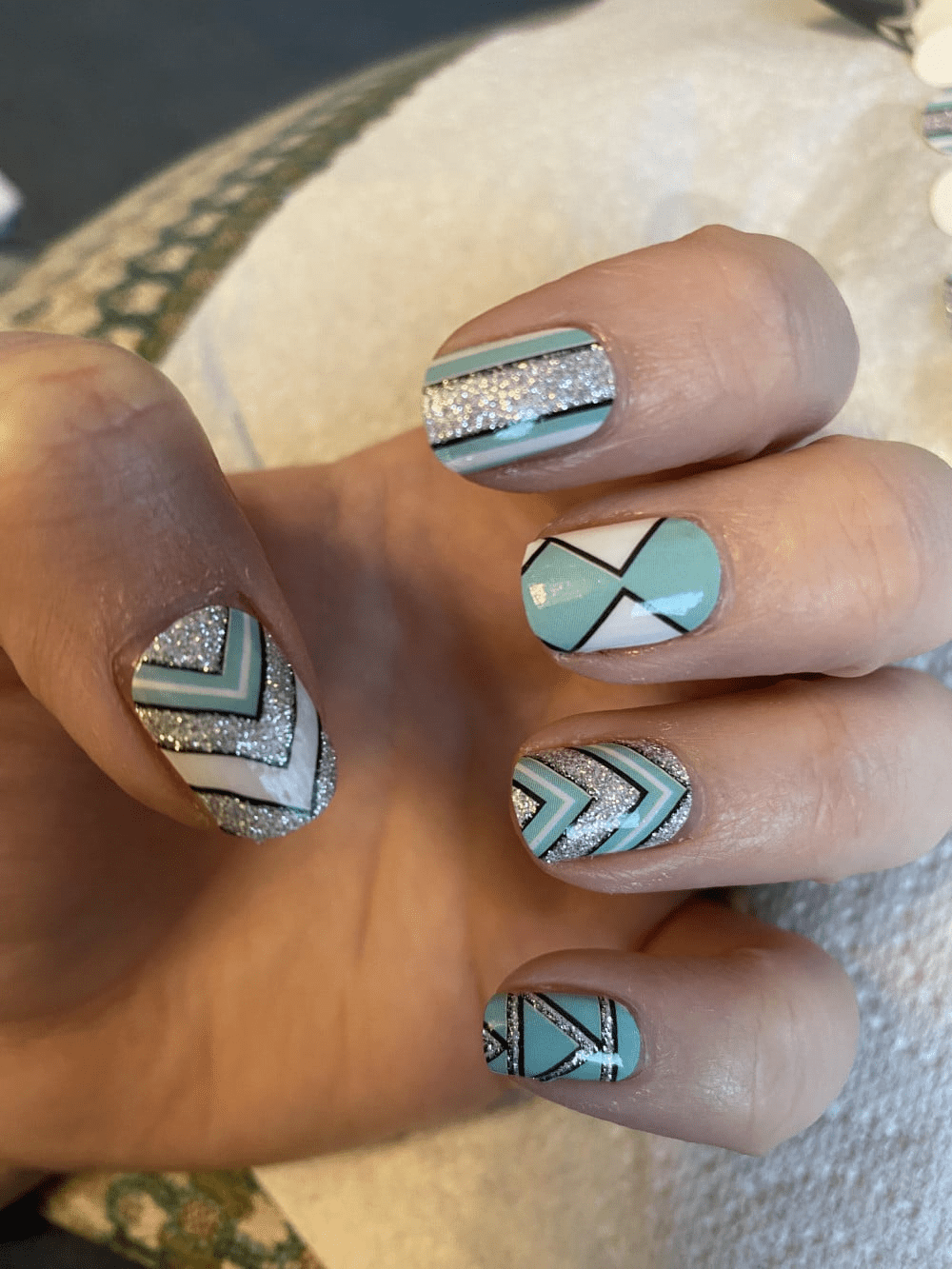 Geometric chevron nail art on hand featuring teal and silver glitter patterns