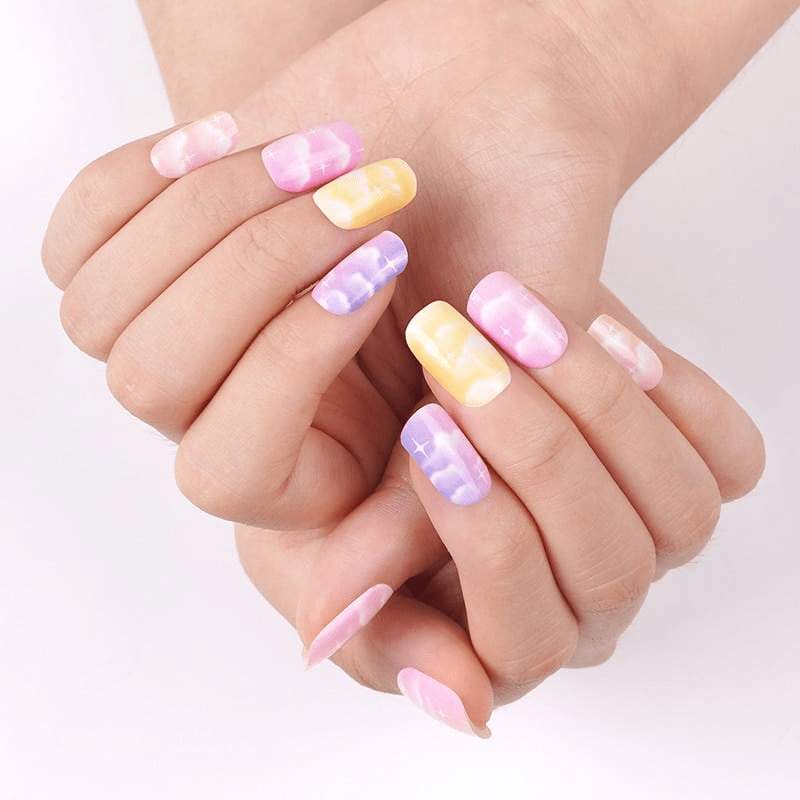 Pastel cloud nail art on hands featuring purple pink yellow nail wraps