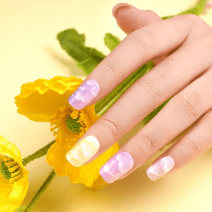 Hand with dreamy cloud nail wraps in purple yellow tones near flowers