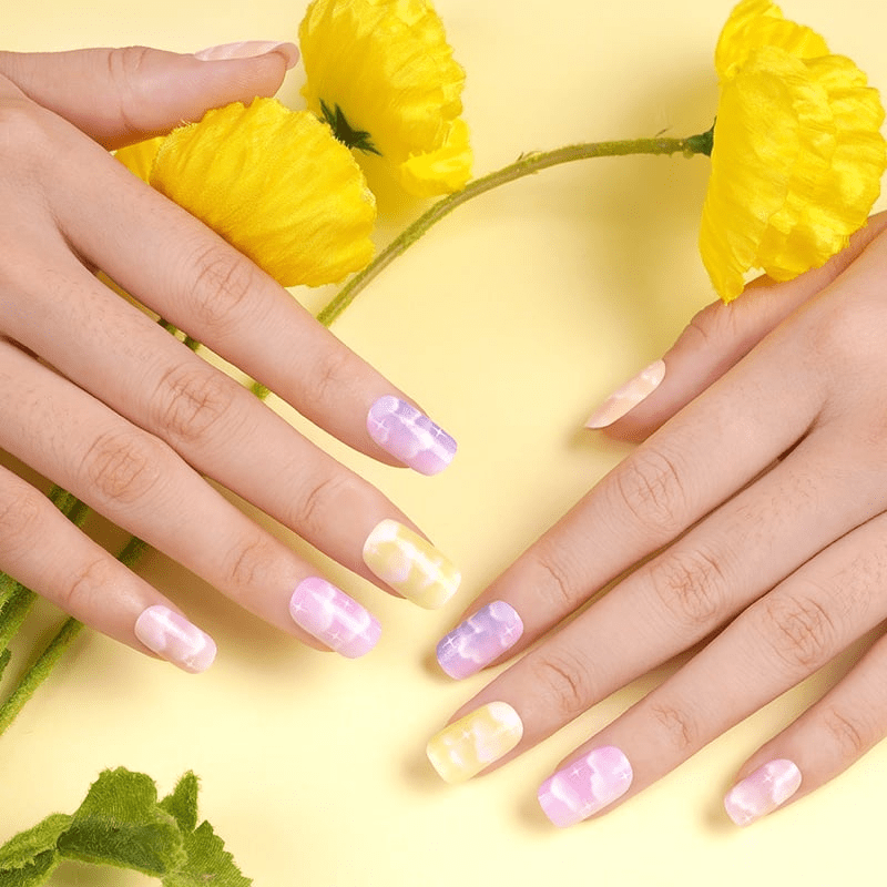 Both hands displaying pastel cloud nail art wraps in purple yellow shades