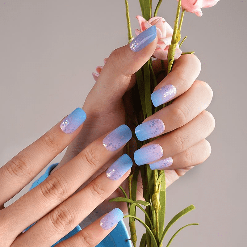 Hand holding flowers wearing blue pink gradient nail wraps with glitter confetti