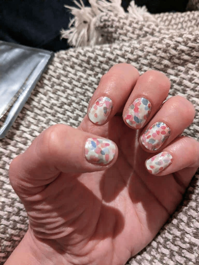 Hand displaying confetti pattern nail wraps with pink blue white dots manicure