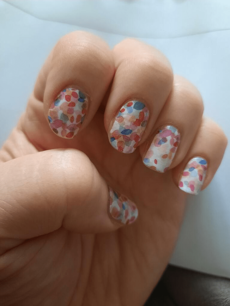 Close-up hand showing multicoloured confetti dot nail wraps at-home manicure