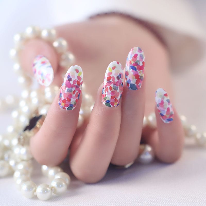Manicured hand wearing confetti nail art wraps with pearl bracelet accessory