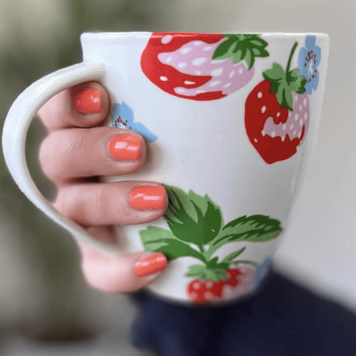 Coral nail wraps manicure on hand holding strawberry patterned mug