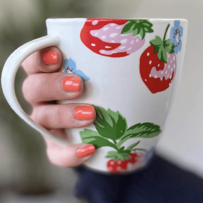 Coral nail wraps manicure on hand holding strawberry patterned mug