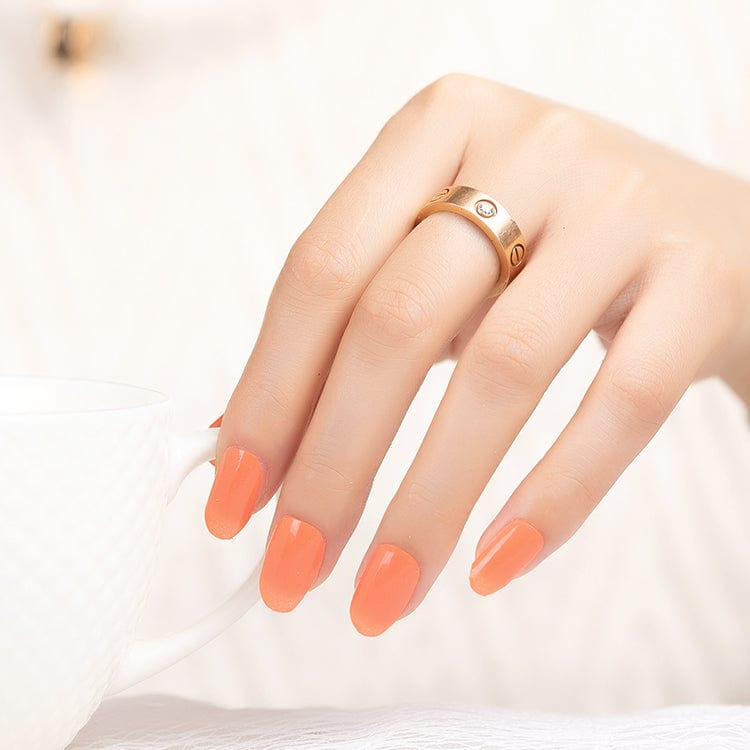 Hand wearing coral orange nail wraps with gold ring showing at-home manicure results