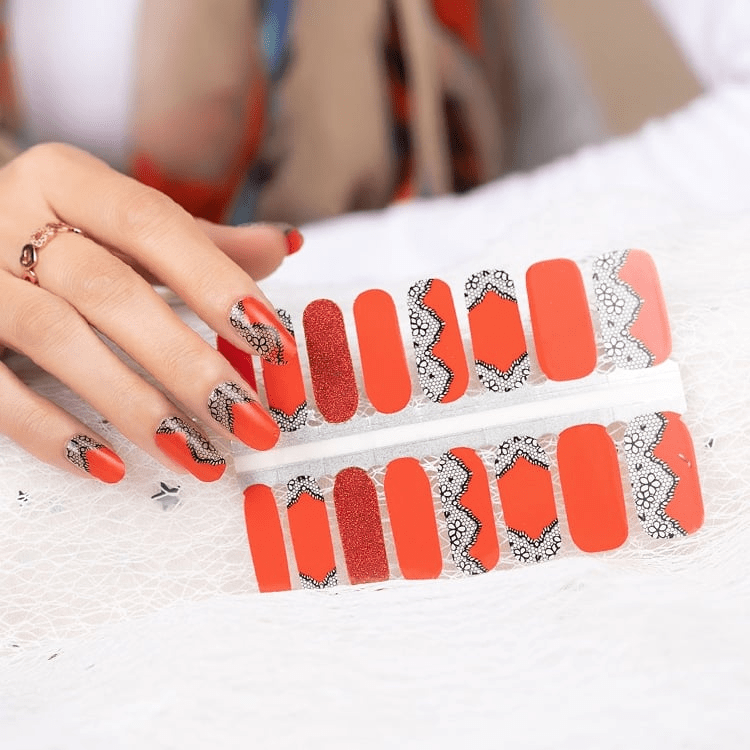 Orange-red nail wraps with black lace trim and glitter accent nail, glossy finish