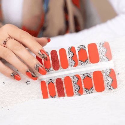 Orange-red nail wraps with black lace trim and glitter accent nail, glossy finish