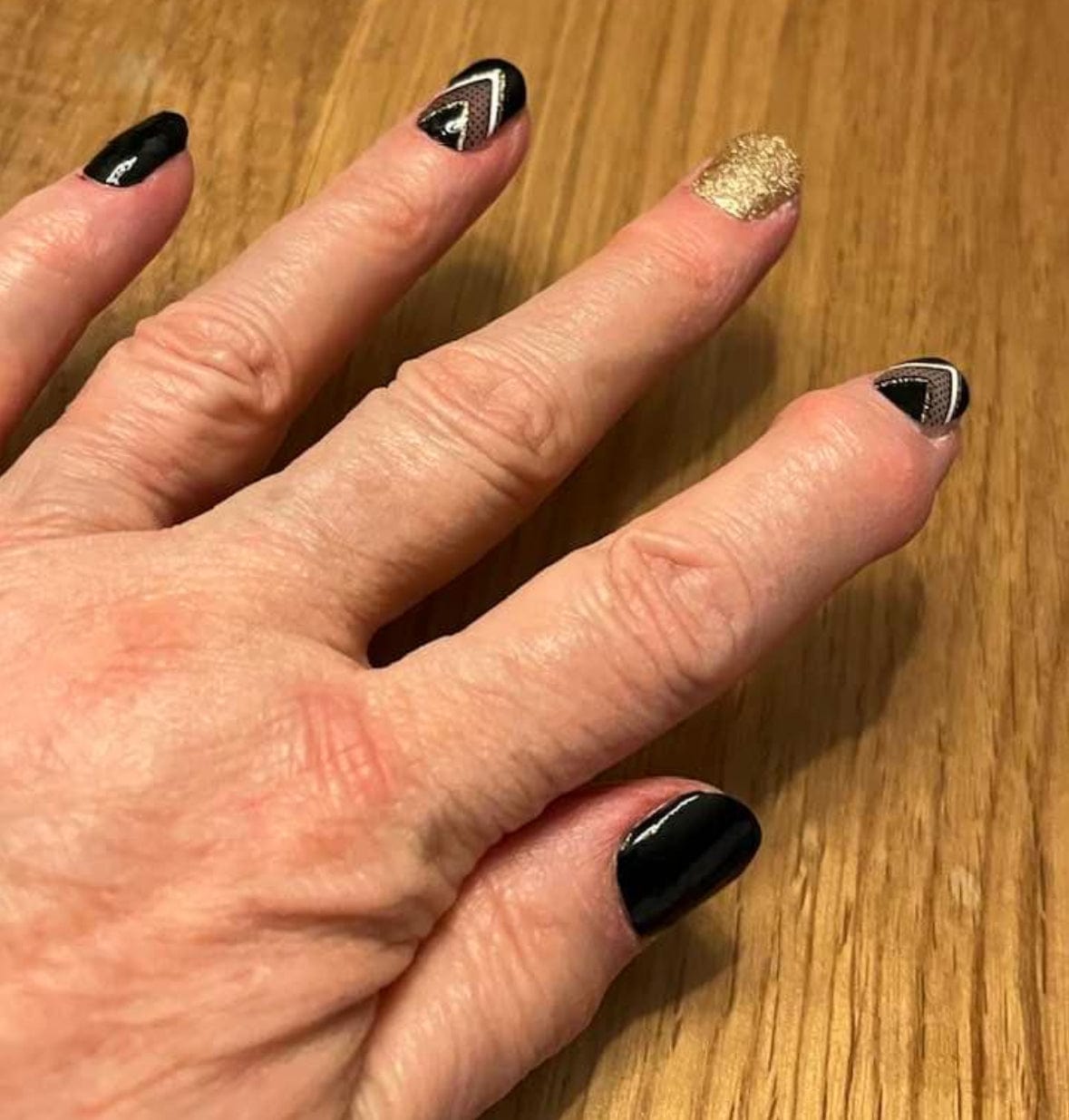 Hand wearing black and gold geometric nail wraps with glittery accent nail for stylish manicure