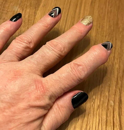 Hand wearing black and gold geometric nail wraps with glittery accent nail for stylish manicure