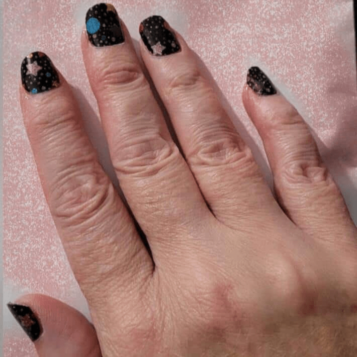 Black nail wraps with multicolour speckles and star accents, galaxy-inspired design