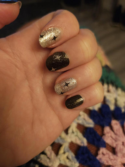 Close-up of black and gold glitter nail wraps with star pattern on fingers