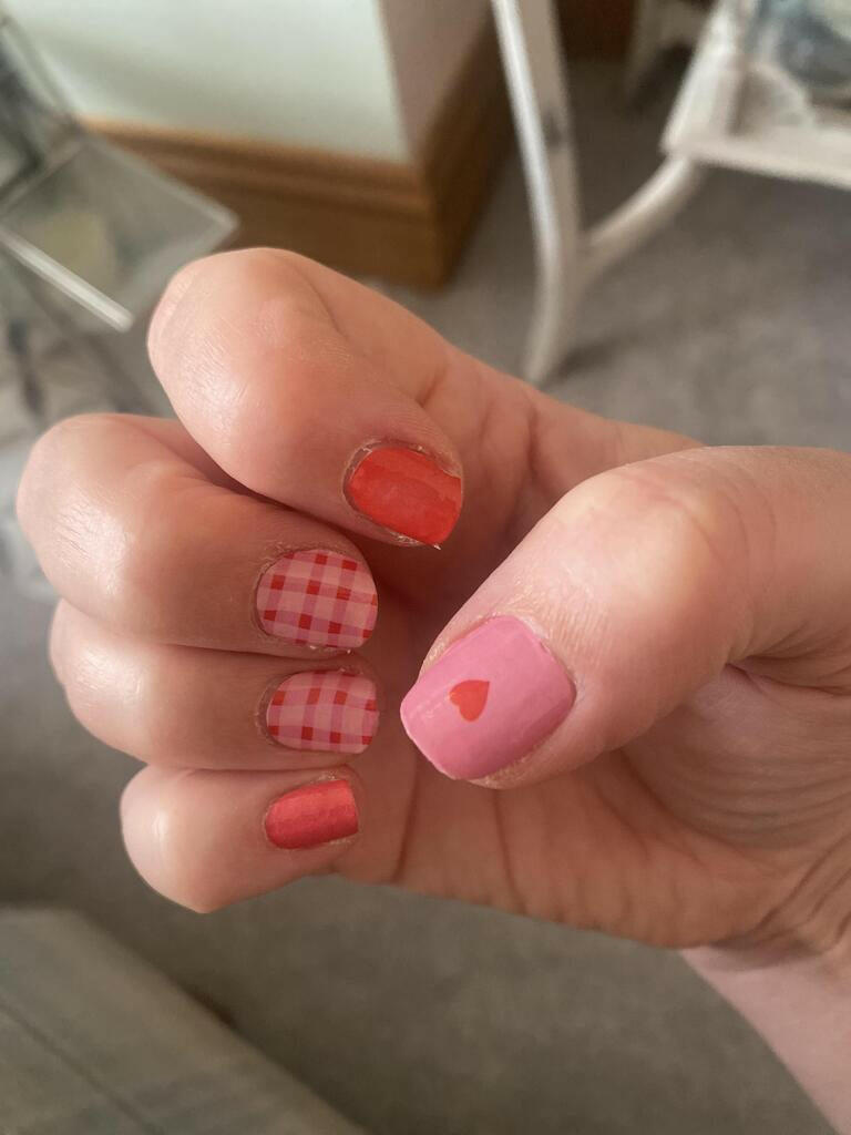 Hand wearing pink gingham and red heart nail wraps for cute manicure