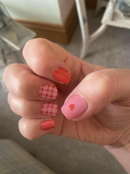 Hand wearing pink gingham and red heart nail wraps for cute manicure