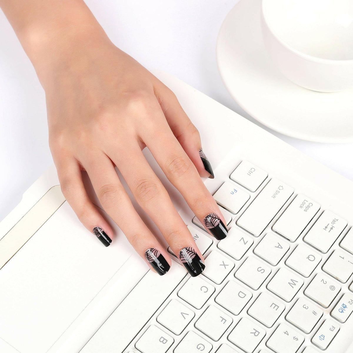 Hand with black spider web nail wraps typing on white keyboard showing gothic nail art