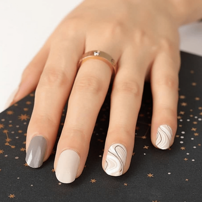 Hand wearing cream marble nail wraps with mixed nude and grey tones