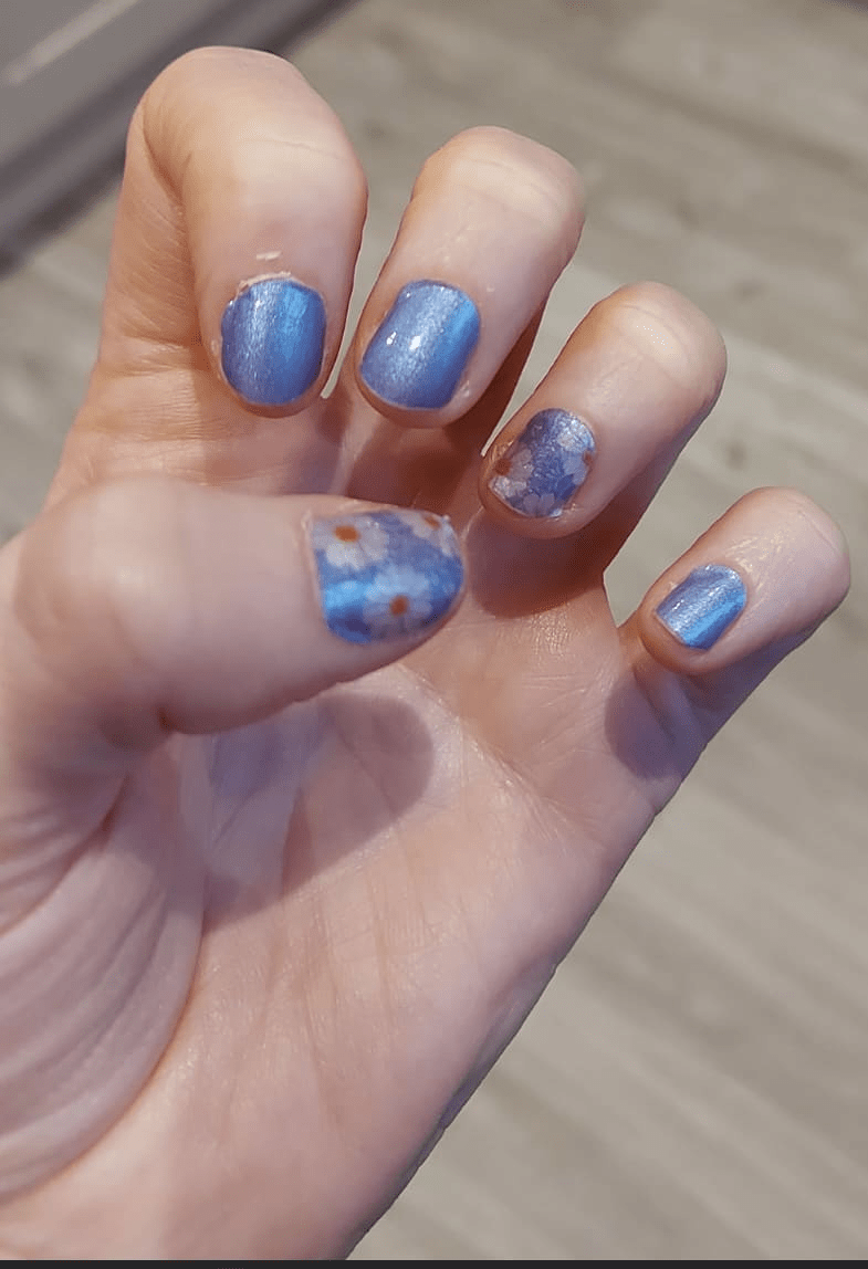 Blue nail wraps with white daisy pattern applied on hand showing glossy finish