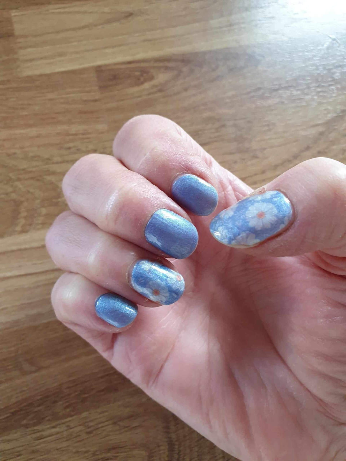 Shimmery blue nail wraps with white daisy floral accents on short round nails