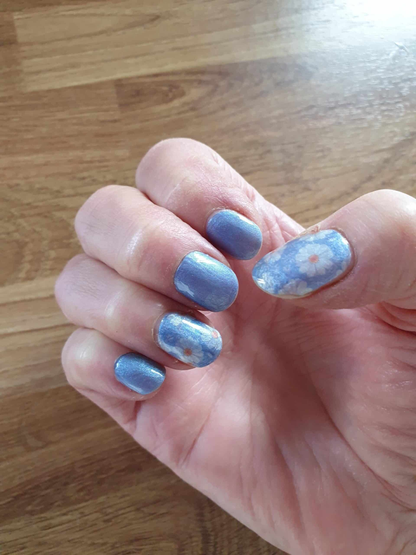 Shimmery blue nail wraps with white daisy floral accents on short round nails