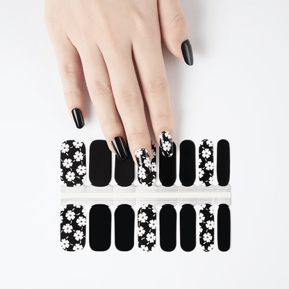 Hand displaying black nails with white daisy print nail wraps and matching wrap sheets