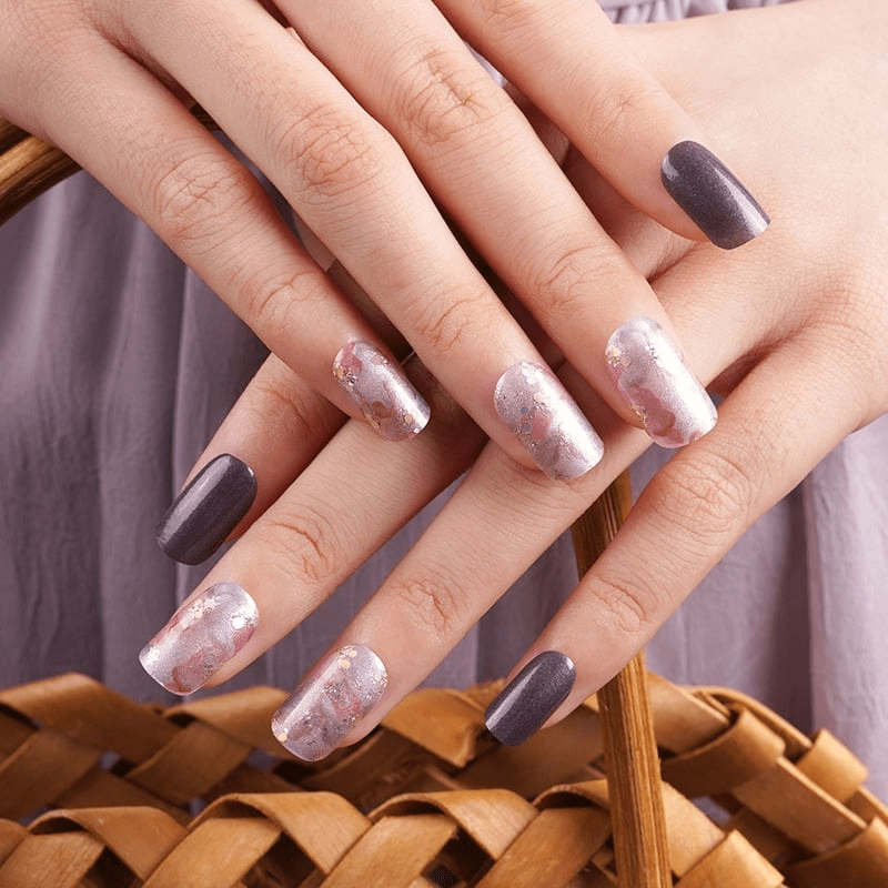 Close-up manicured hands displaying abstract watercolour nail wraps in coral and brown tones