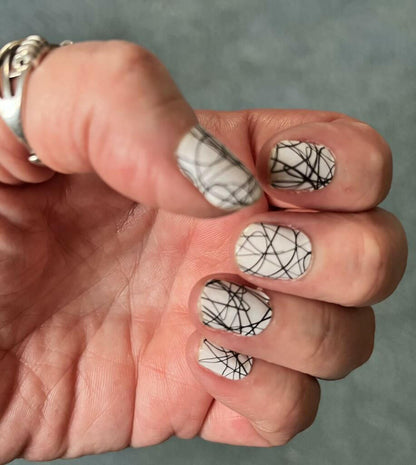 Hand wearing white nail wraps with black abstract line pattern geometric design