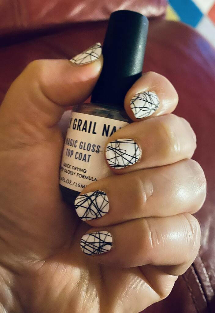 White nail wraps with black scribble line design, hand holding Magic Gloss top coat bottle.