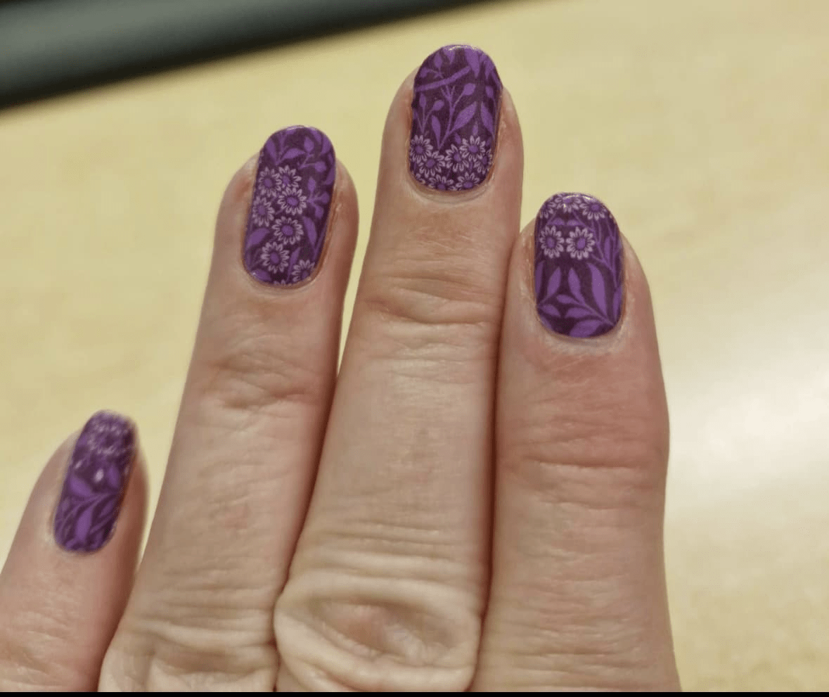Hand wearing purple floral nail wraps with botanical leaf and daisy design