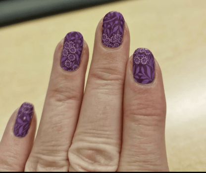 Hand wearing purple floral nail wraps with botanical leaf and daisy design