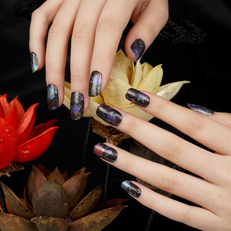 Dark garden nail wraps with metallic floral design on hands holding decorative flowers