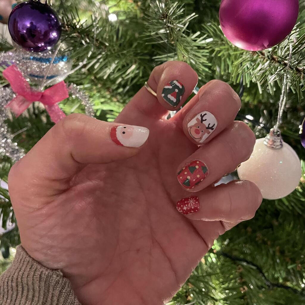 Christmas nail wraps on hand with Santa, reindeer and red glitter designs near Christmas tree