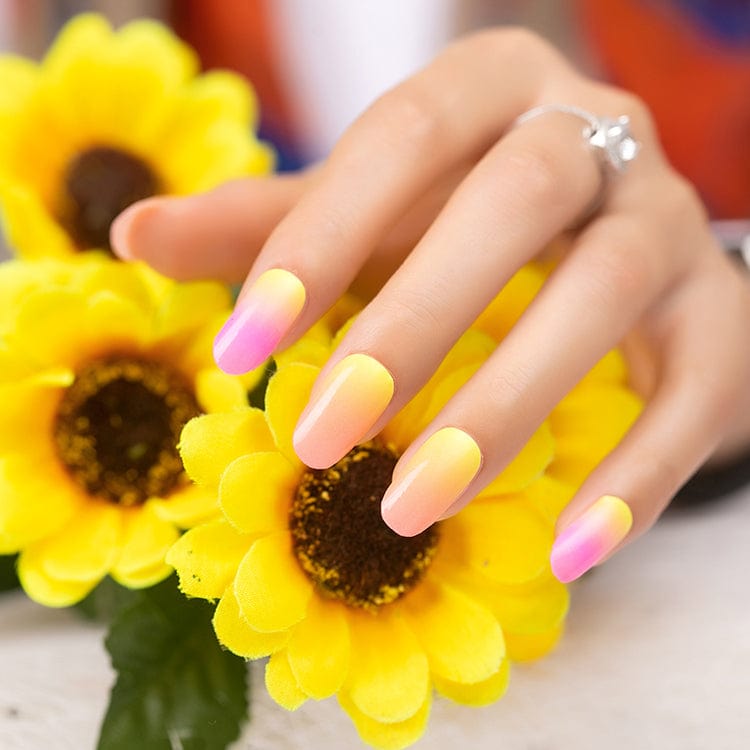 Hand wearing bright yellow to pink gradient nail wraps holding sunflower