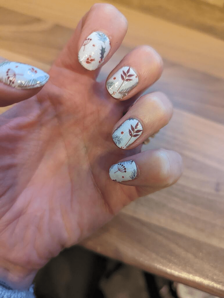 Festive nail wraps on hand showing white Christmas design with holly leaves and berries