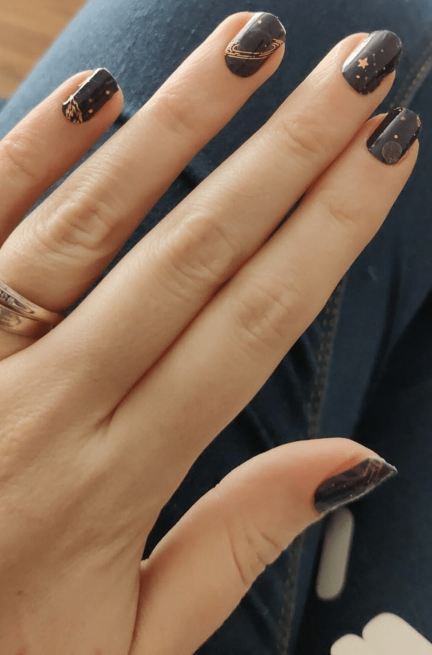 Black nail wraps with gold celestial design, stars, planets and constellations