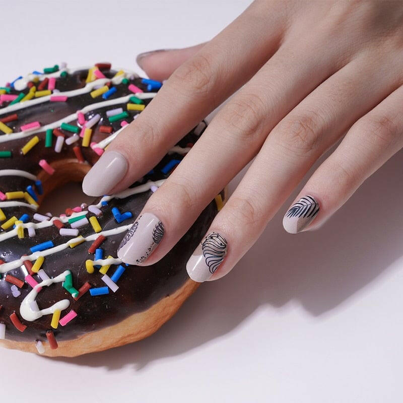 Hand with brown feather nail art wraps reaching for chocolate sprinkle donut