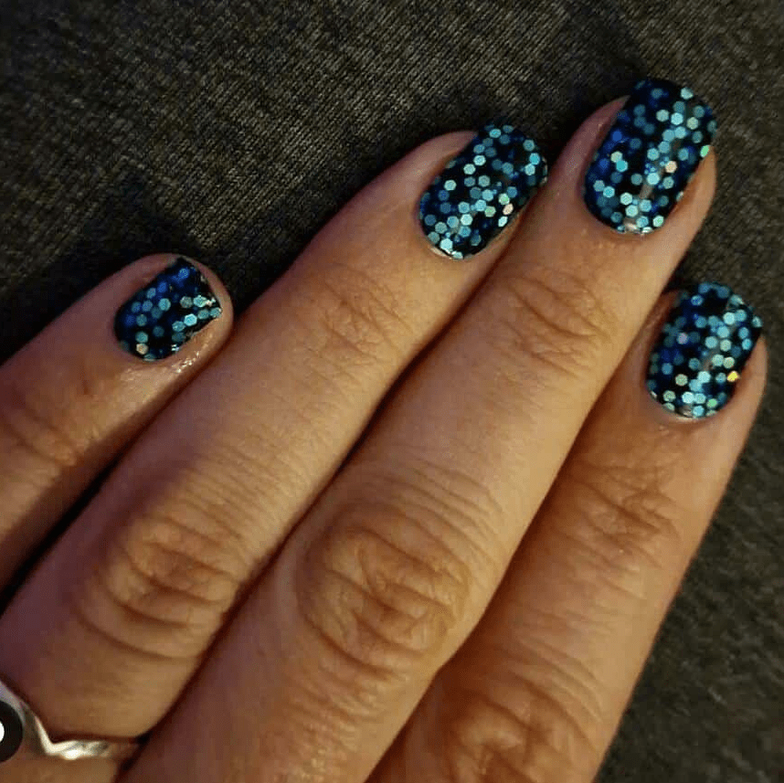 Close-up hand with dark blue glitter nail wraps featuring holographic party finish