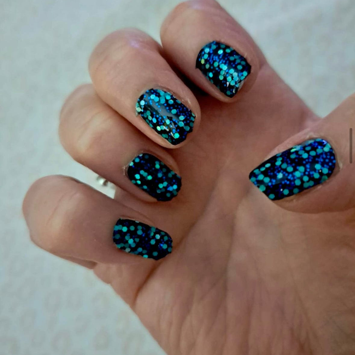 Hand wearing blue teal glitter nail wraps with hexagon sequin pattern for statement nails