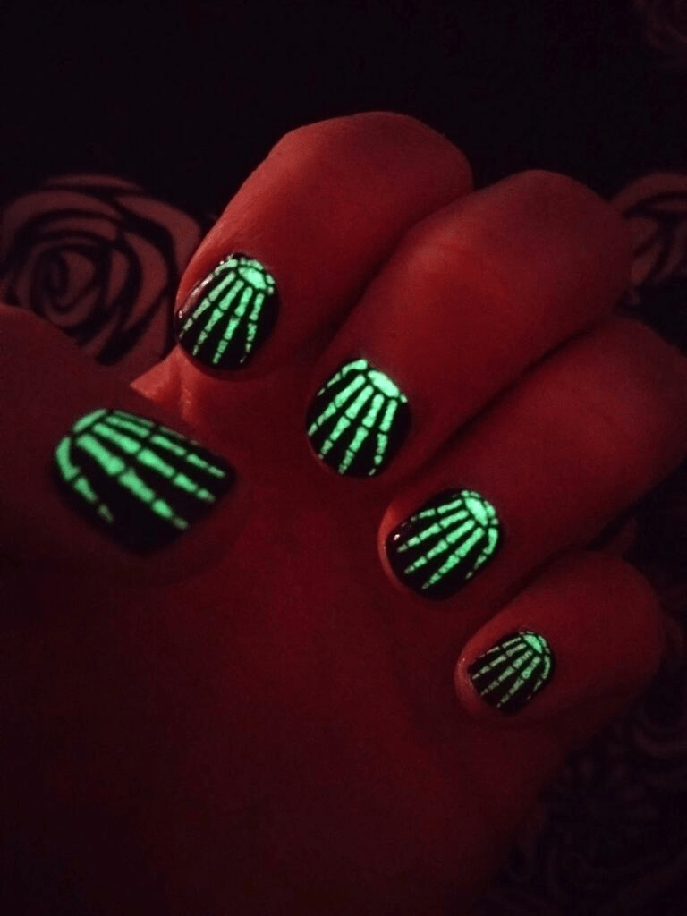 Glow-in-the-dark skeleton nail wraps glowing green in darkness for Halloween nail art