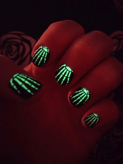 Glow-in-the-dark skeleton nail wraps glowing green in darkness for Halloween nail art