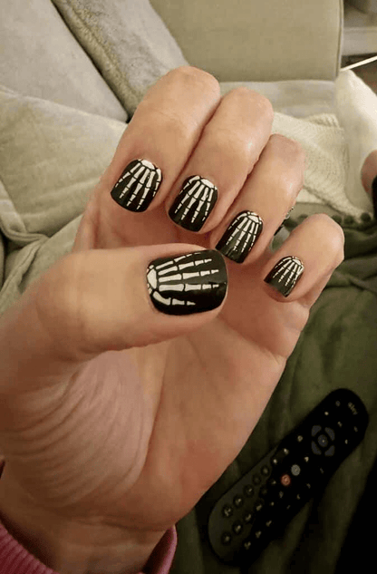 Hand displaying black nail wraps with white skeleton bone design for Halloween manicure