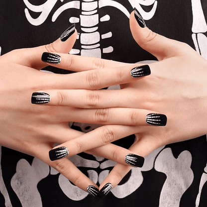 Gothic skeleton bone pattern nail wraps on hands against black Halloween costume background
