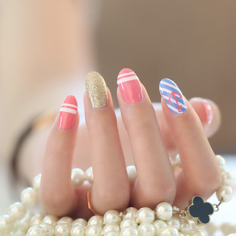 Manicured hand displaying coral pink blue striped nautical nail wraps with gold glitter nail
