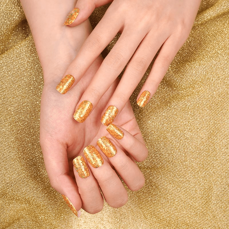 Two hands showcasing gold glitter nail wraps on matching glittery background for luxury manicure
