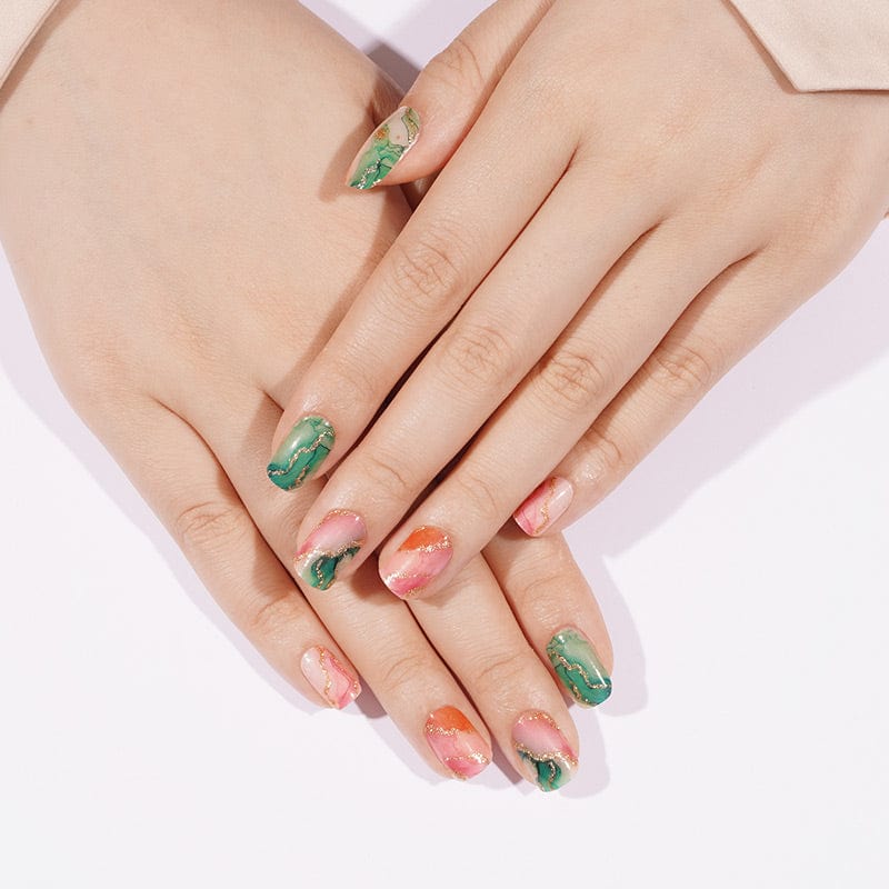Hands displaying green orange marble nail wraps with gold accents manicure design