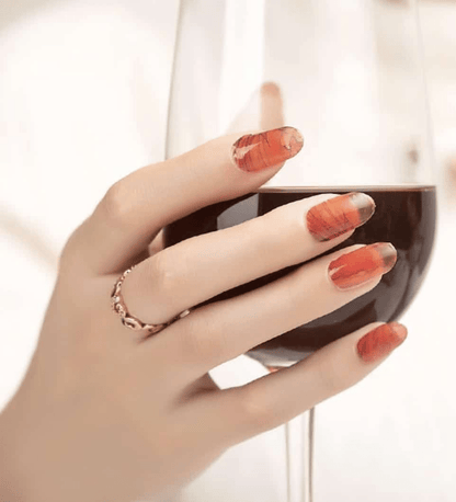 Hand holding mug wearing burnt orange marble nail wraps with terracotta stone finish
