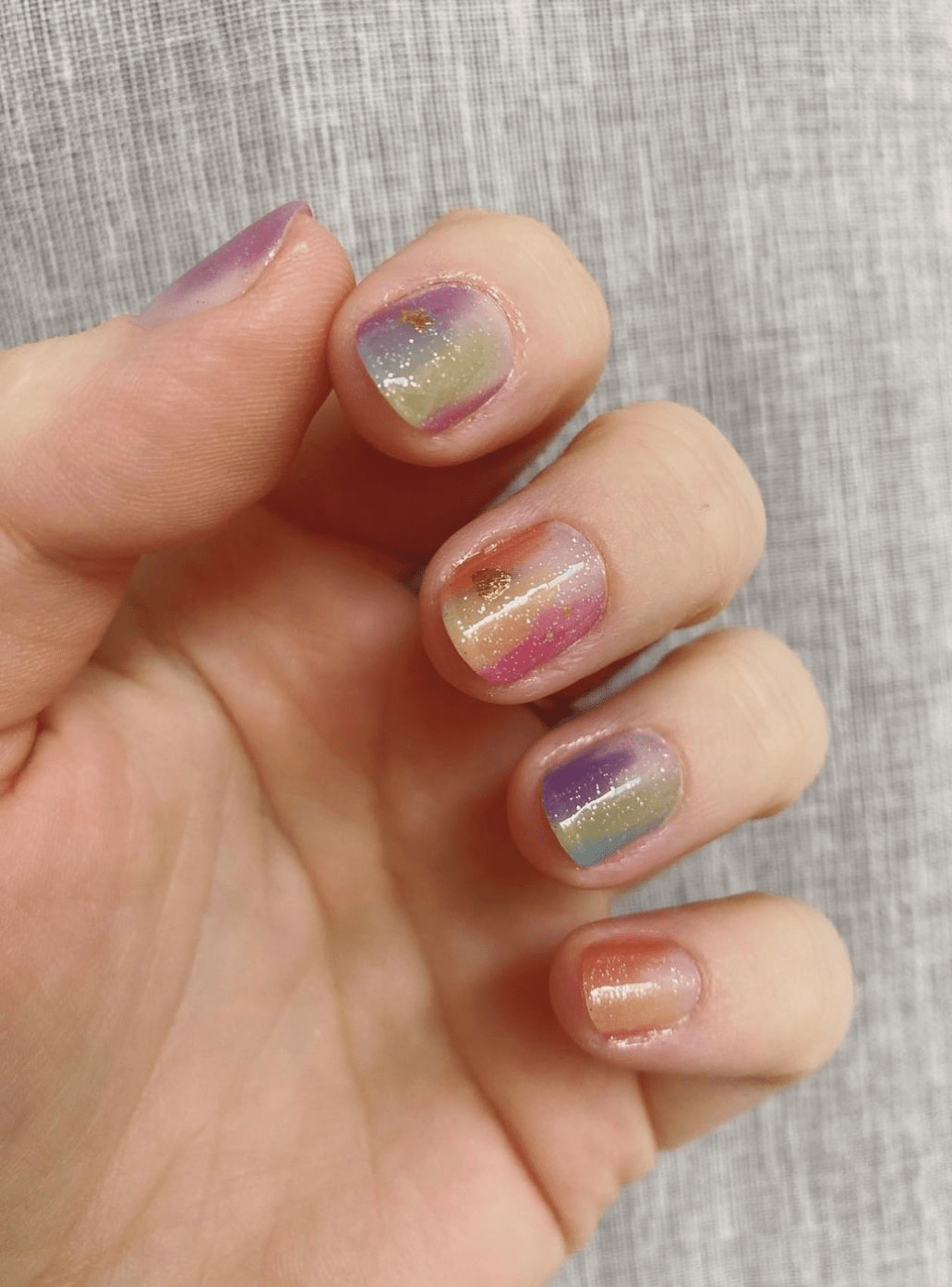 Hand wearing multicoloured holographic nail wraps with pink purple gold shimmer gradient finish