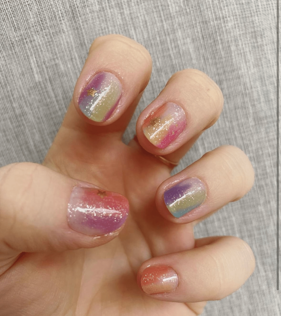 Close up hand showing iridescent nail wraps with pink purple gold holographic ombre design