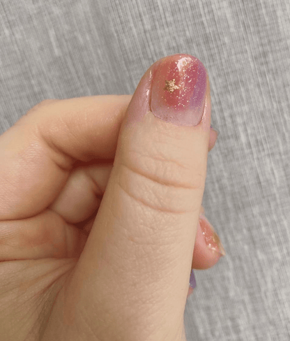 Hand showing pink purple gradient nail wraps with gold shimmer and holographic finish